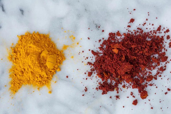 Two piles of turmeric powder, one yellow and one red